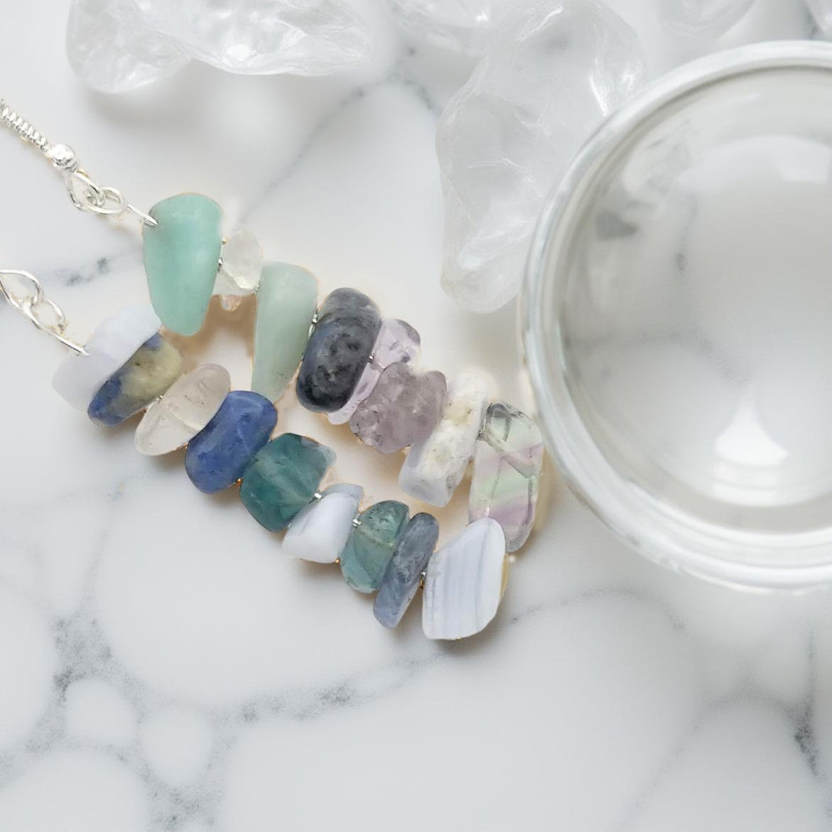 Assorted chipped crystals including sodalite, blue lace agate, amazonite, clear quartz and green fluorite. Hanging on a silver toned fishhook, with the gemstones a-lined on a 2 1/4th inch drop in a random but complementary order.