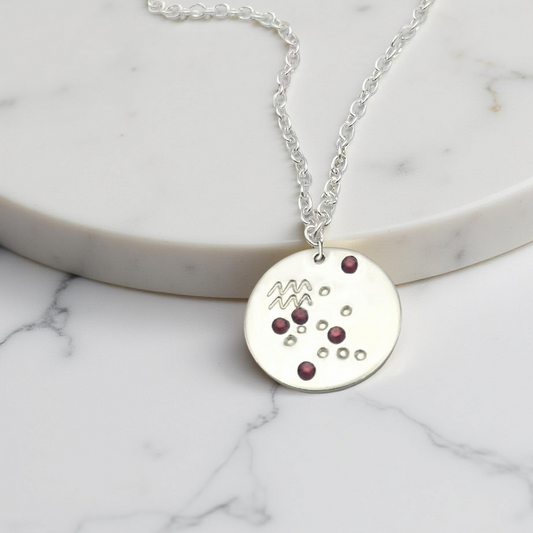 February Aquarius necklace pendant with hand set amethyst colored glass rhinestones forming the constellation of Aquarius. Hand stamped with the zodiac symbol for Aquarius, on a 3/4th of an inch silver toned circle hanging from a silver toned chain.