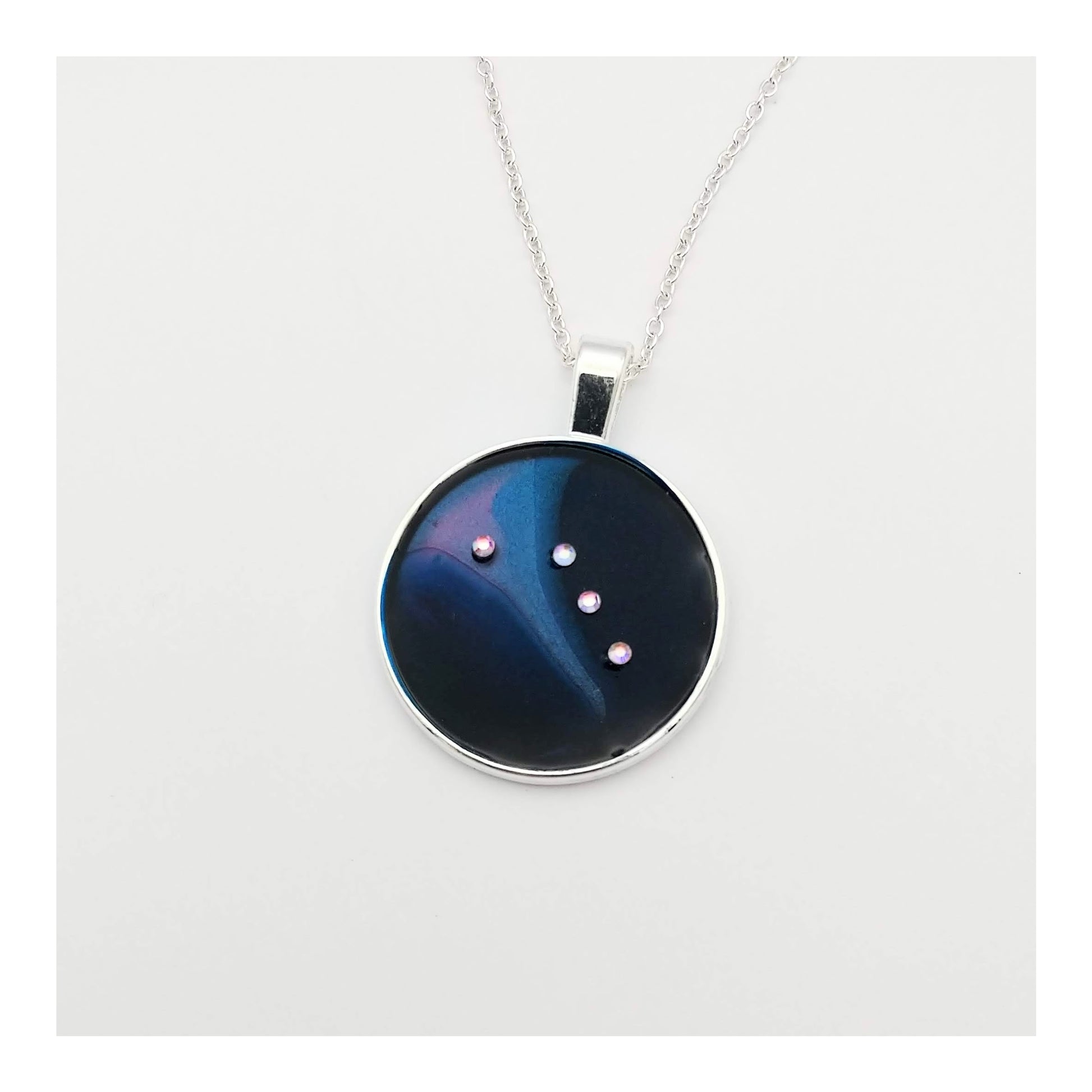 Dark blue with iridescent sparkling swirls of  pinks, purples, silver, and monochromatic shades of blue enamel. With handset Aurora Borealis rhinestones to represent the star of the constellation of Aries. The pendant is 1 inch silver toned with a 1/4th inch bail on a silver toned chain..  