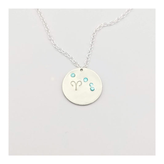 March Aries necklace pendant with hand set aquamarine colored glass rhinestones forming the constellation of Aries. Hand stamped with the zodiac symbol for aries, on a 3/4th of an inch silver toned circle hanging from a silver toned chain.