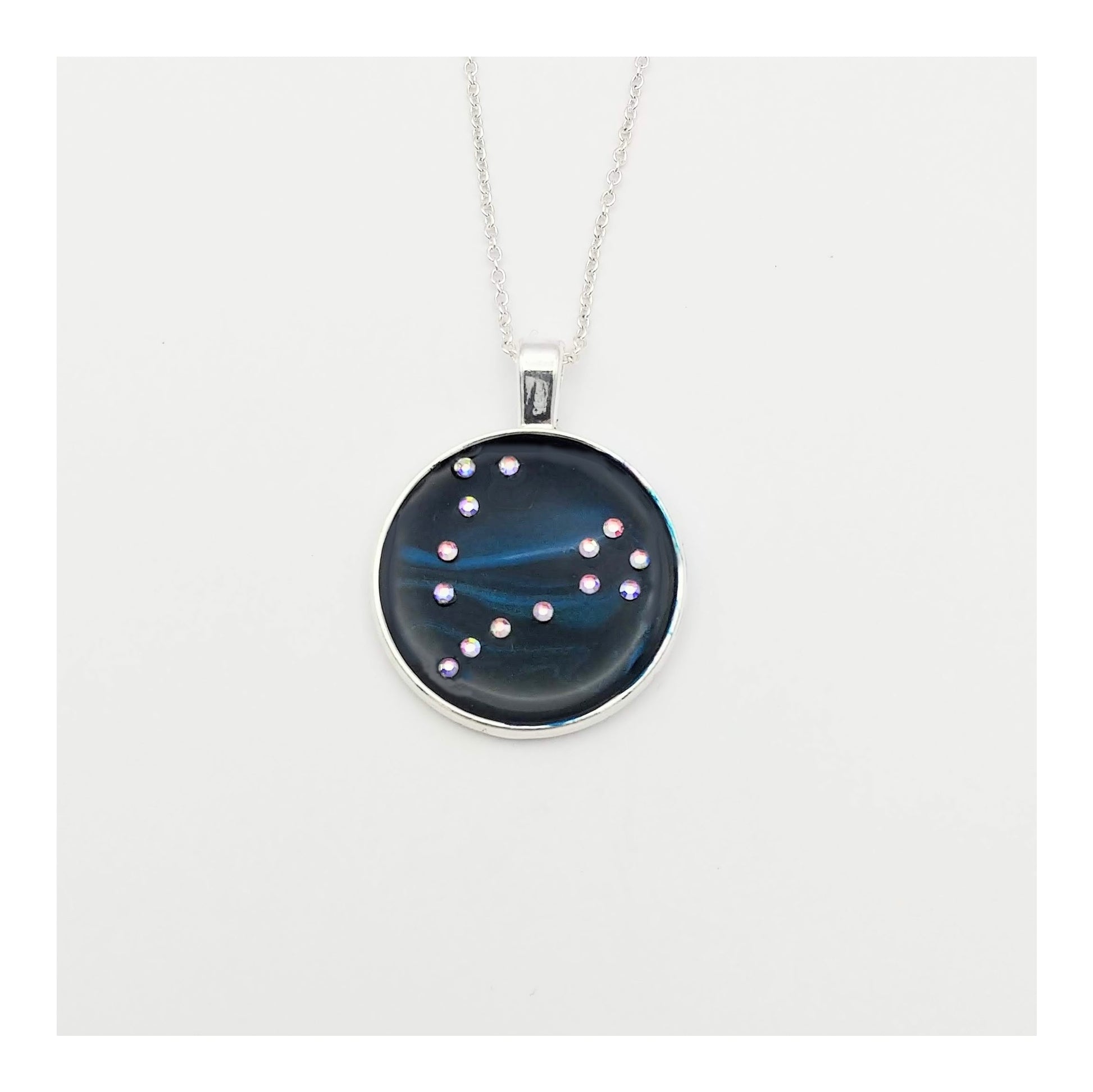 Dark blue with iridescent sparkling swirls of pinks, purples, silver, and monochromatic shades of blue enamel. With handset Aurora Borealis rhinestones to represent the star of the constellation of Pisces. The pendant is 1 inch silver toned with a 1/4th inch bail on a silver toned chain.