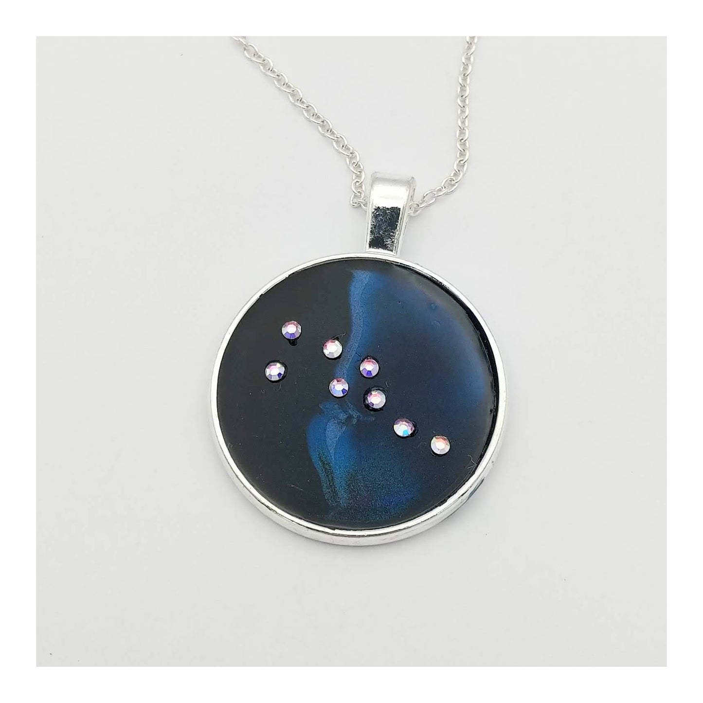 Dark blue with iridescent sparkling swirls of pinks, purples, silver, and monochromatic shades of blue enamel. With handset Aurora Borealis rhinestones to represent the star of the constellation of Taurus. The pendant is 1 inch silver toned with a 1/4th inch bail on a silver toned chain.