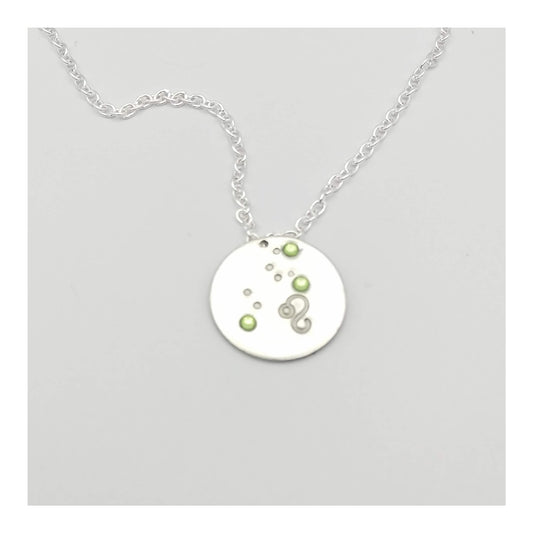 August Leo necklace pendant with hand set peridot colored glass rhinestones forming the constellation of Leo. Hand stamped with the zodiac symbol for Leo, on a 3/4th of an inch silver toned circle hanging from a silver toned chain.