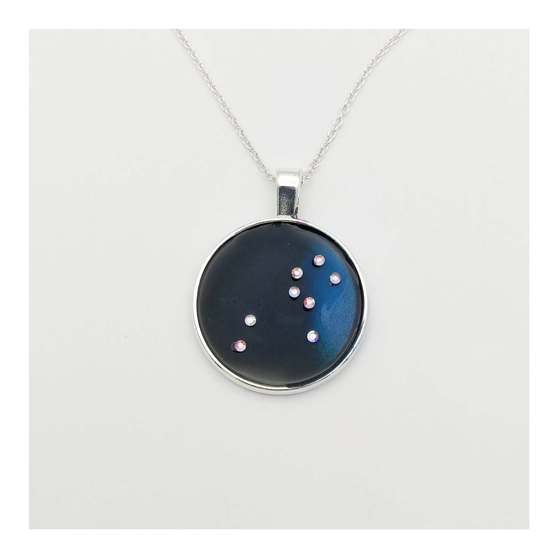 Dark blue with iridescent sparkling swirls of pinks, purples, silver, and monochromatic shades of blue enamel. With handset Aurora Borealis rhinestones to represent the star of the constellation of Leo. The pendant is 1 inch silver toned with a 1/4th inch bail on a silver toned chain.