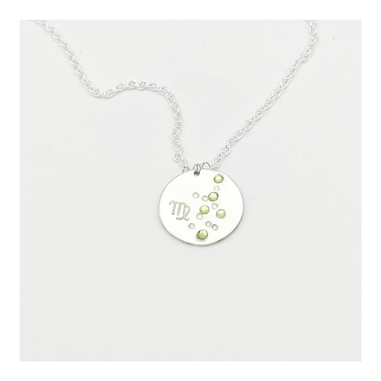 August Virgo necklace pendant with hand set peridot colored glass rhinestones forming the constellation of Virgo. Hand stamped with the zodiac symbol for Virgo, on a 3/4th of an inch silver toned circle hanging from a silver toned chain.