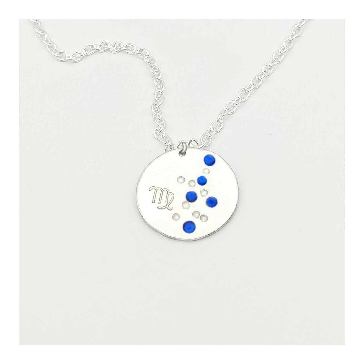 September Virgo necklace pendant with hand set sapphire colored glass rhinestones forming the constellation of Virgo. Hand stamped with the zodiac symbol for Virgo, on a 3/4th of an inch silver toned circle hanging from a silver toned chain.