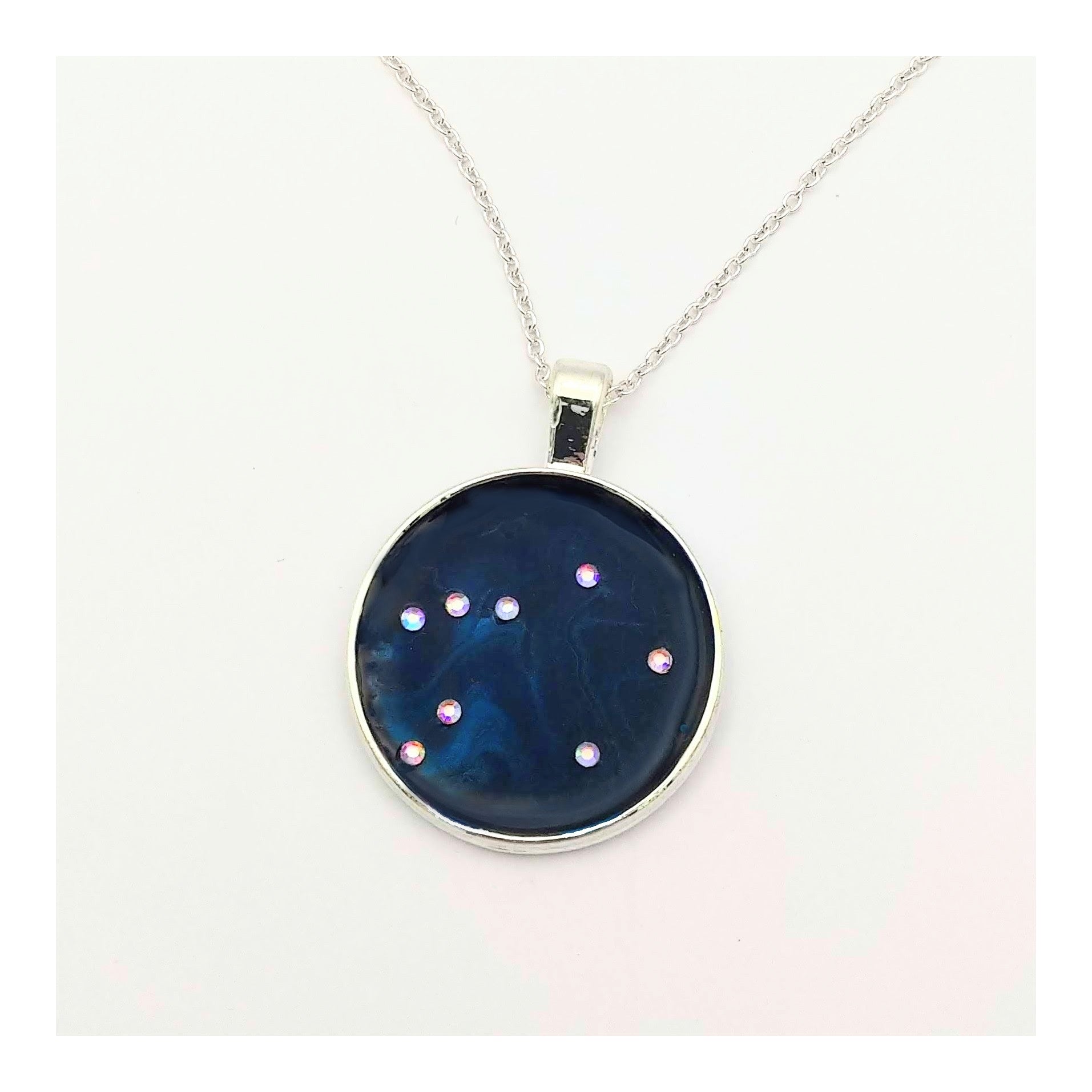 Dark blue with iridescent sparkling swirls of pinks, purples, silver, and monochromatic shades of blue enamel. With handset Aurora Borealis rhinestones to represent the star of the constellation of Libra. The pendant is 1 inch silver toned with a 1/4th inch bail on a silver toned chain.