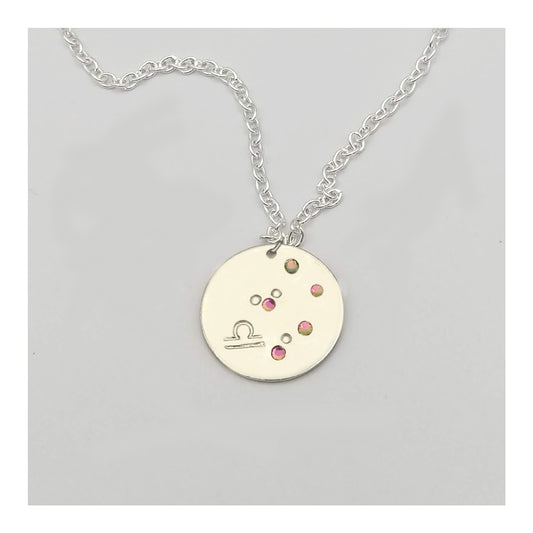 October Libra necklace pendant with hand set tourmaline colored glass rhinestones forming the constellation of Libra. Hand stamped with the zodiac symbol for Libra, on a 3/4th of an inch silver toned circle hanging from a silver toned chain.