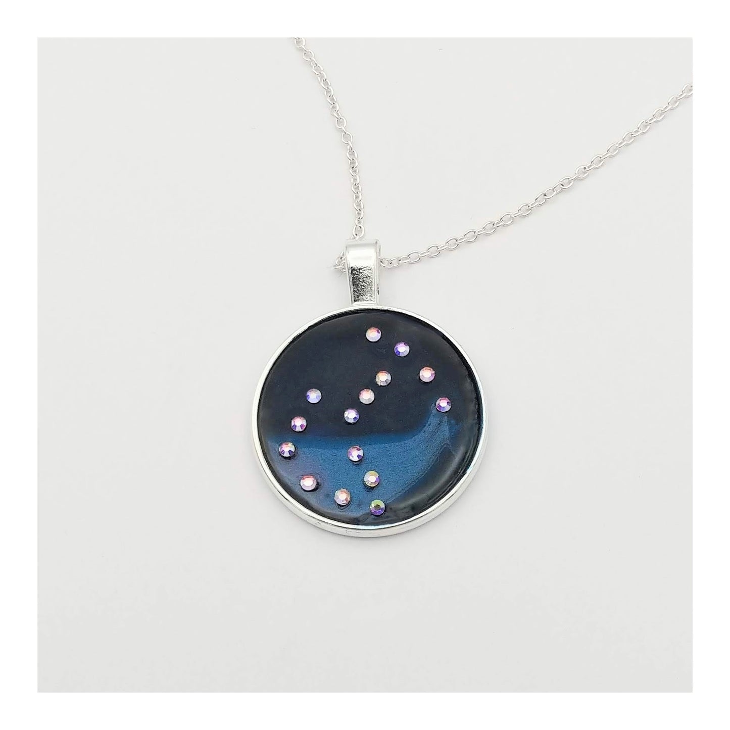 Dark blue with iridescent sparkling swirls of pinks, purples, silver, and monochromatic shades of blue enamel. With handset Aurora Borealis rhinestones to represent the star of the constellation of Scorpio. The pendant is 1 inch silver toned with a 1/4th inch bail on a silver toned chain.