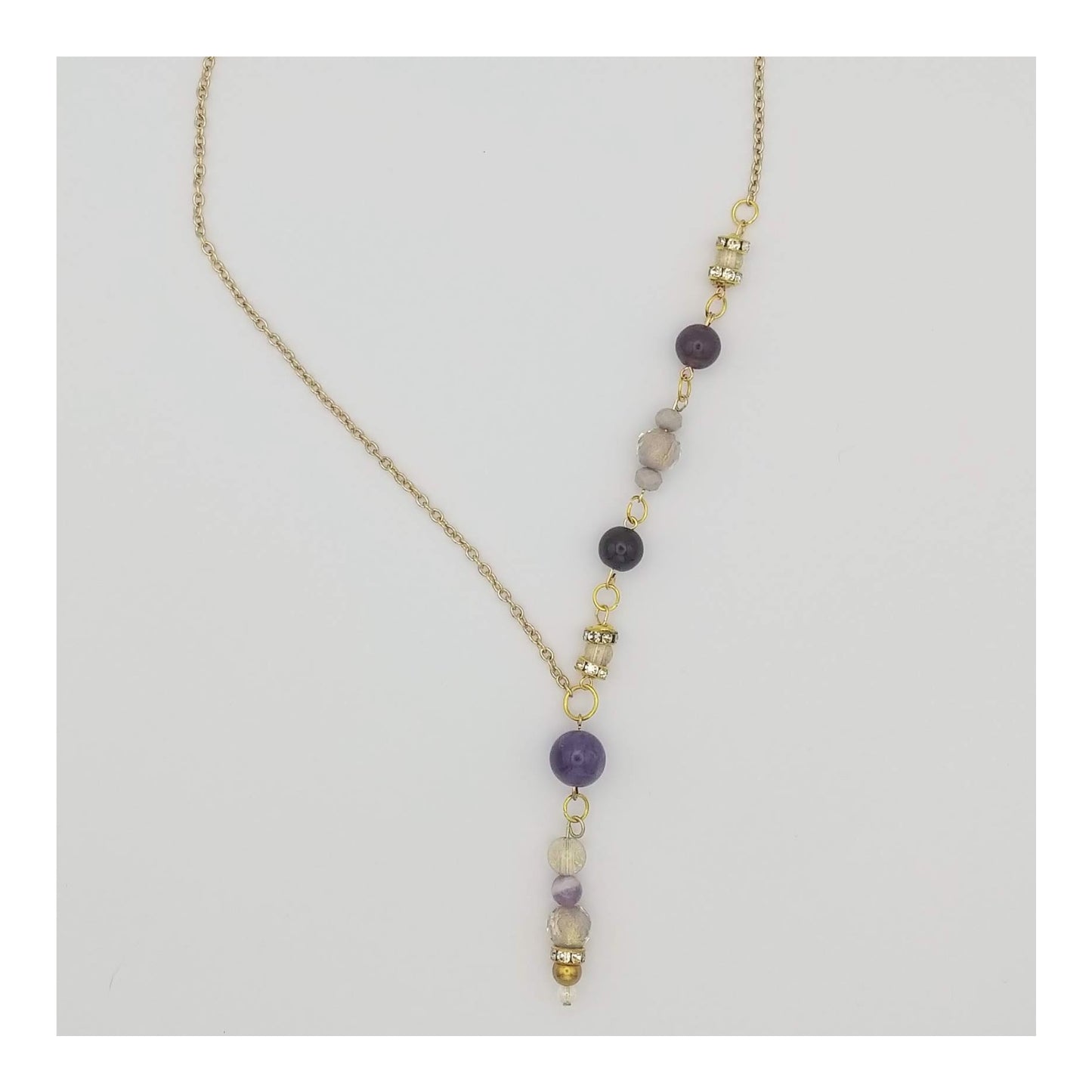 Amethyst round beads with lavender and gold colored accents down one side of the gold toned necklace and a 2 ¼ inch drop. The other side of the necklace is a plain gold toned chain, equaling 18 inches around.  