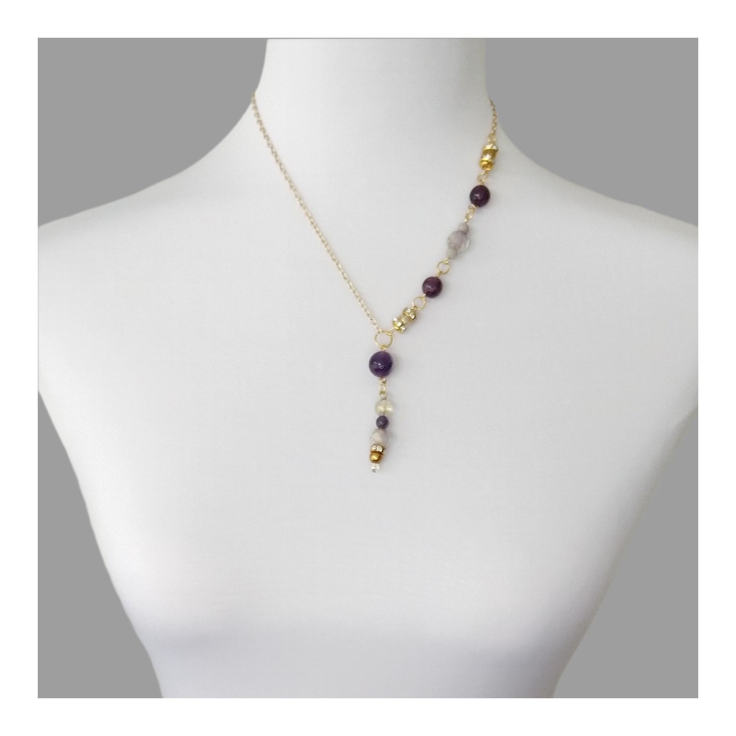 Amethyst round beads with lavender and gold colored accents down one side of the gold toned necklace and a 2 ¼ inch drop. The other side of the necklace is a plain gold toned chain, equaling 18 inches around.  