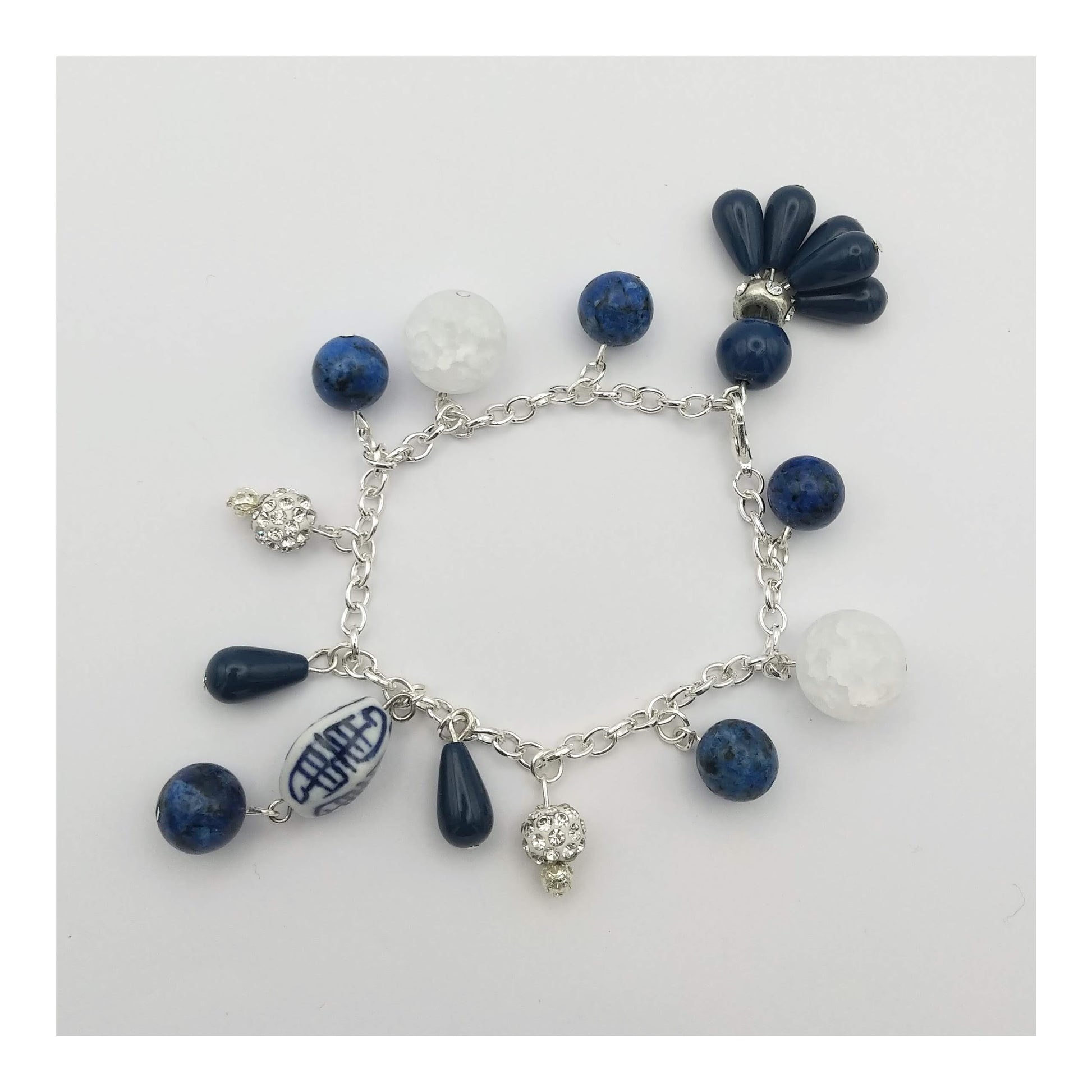 Silver toned charm bracelet with round lapis, cracked clear to white quartz, oblong white and blue porcelain bead and round blue beads with matching teardrop tassel charms. Hanging on a 7 ½ inch adjustable bracelet. 