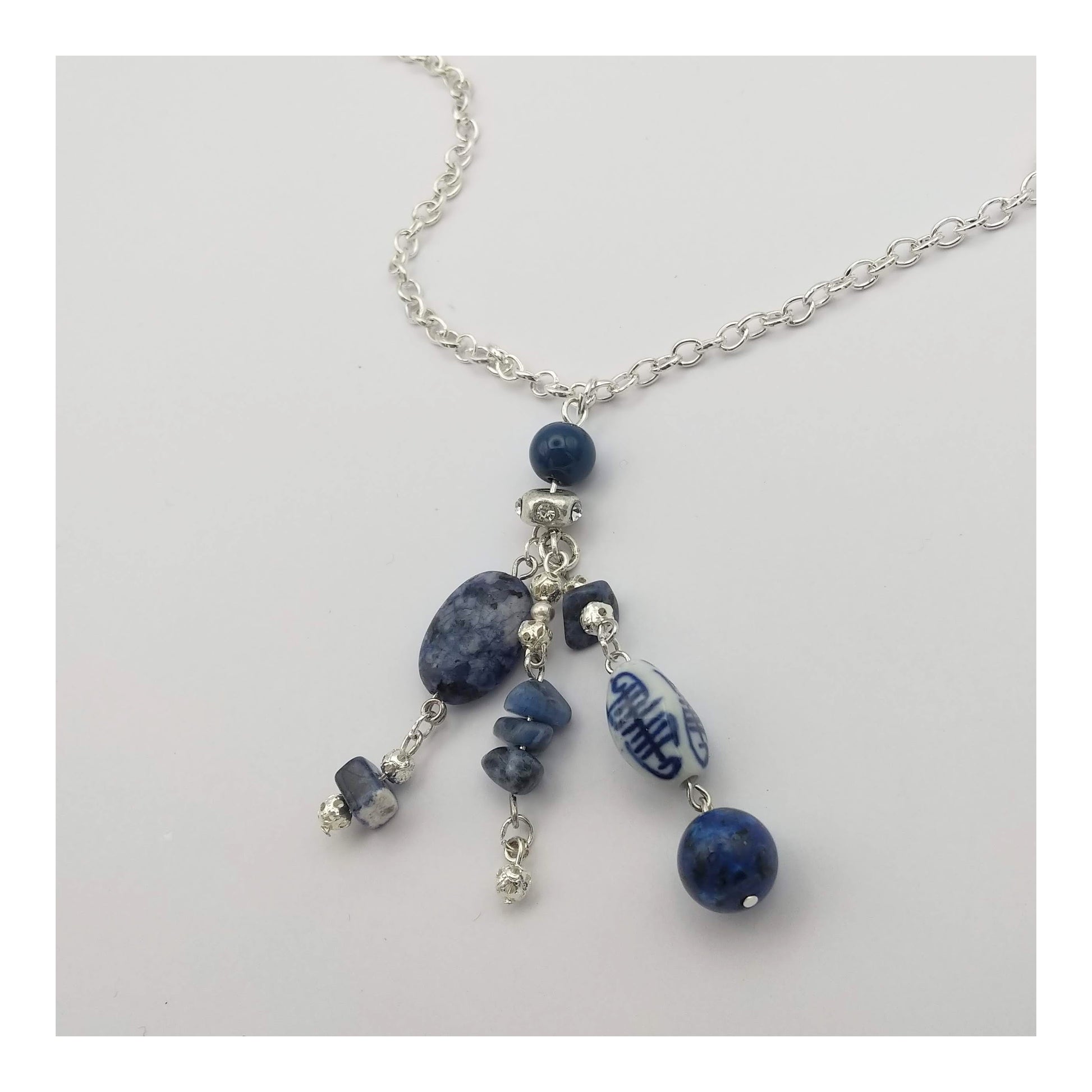 Silver toned 16 inch chain adorn with 3 inch drop hand strung tassel with oval and chipped sodalite, round lapis lazuli, oblong white and blue porcelain and other assorted blue and silver toned beads.  