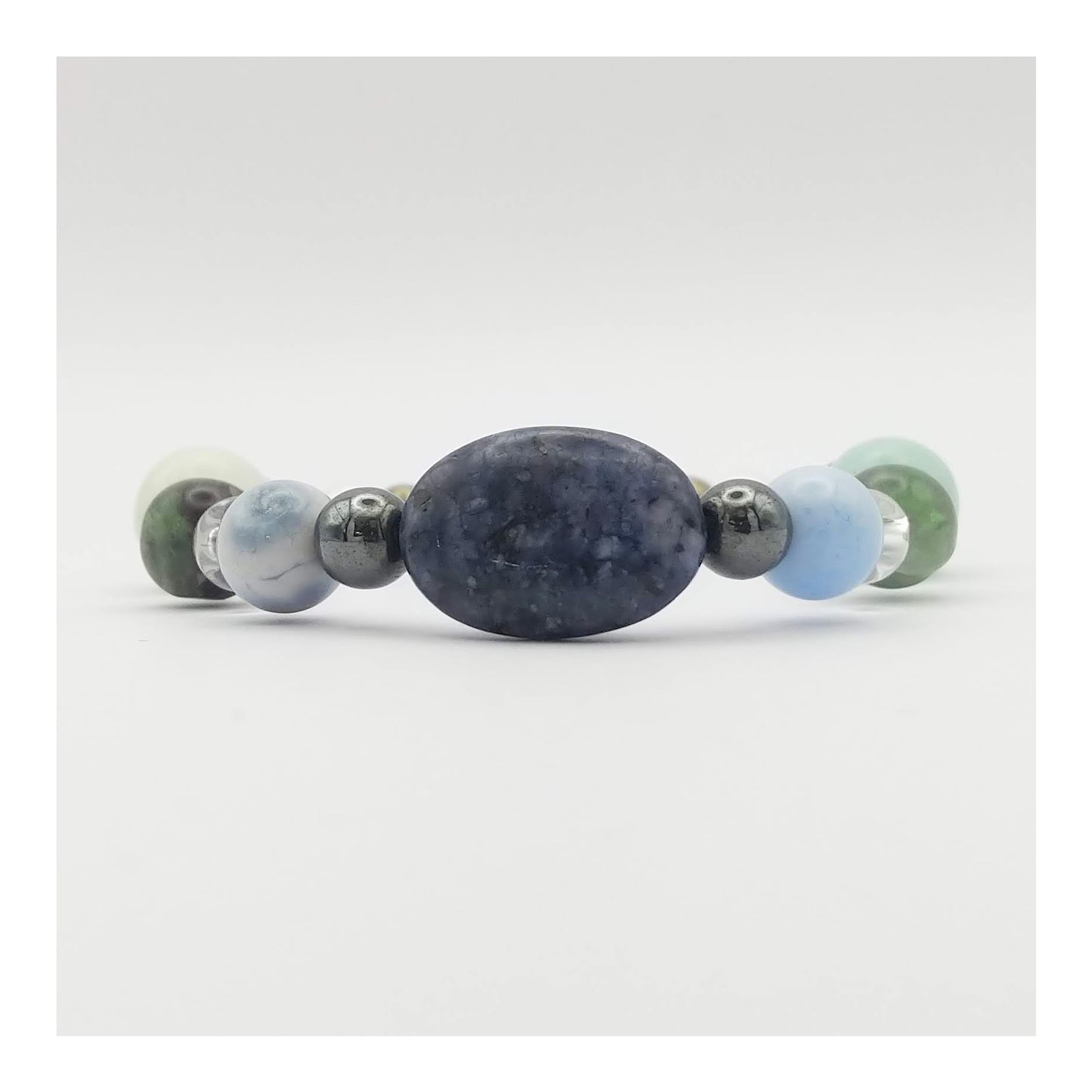 Mercury retrograde elastic bracelet with an oval blue sodalite bead at the center with other crystals such as blue lace agate, clear quartz, green and purple fluorite and other gemstones in a symmetrical pattern. In soothing cool tones  along with hematite and pyrite which have a metallic finish.