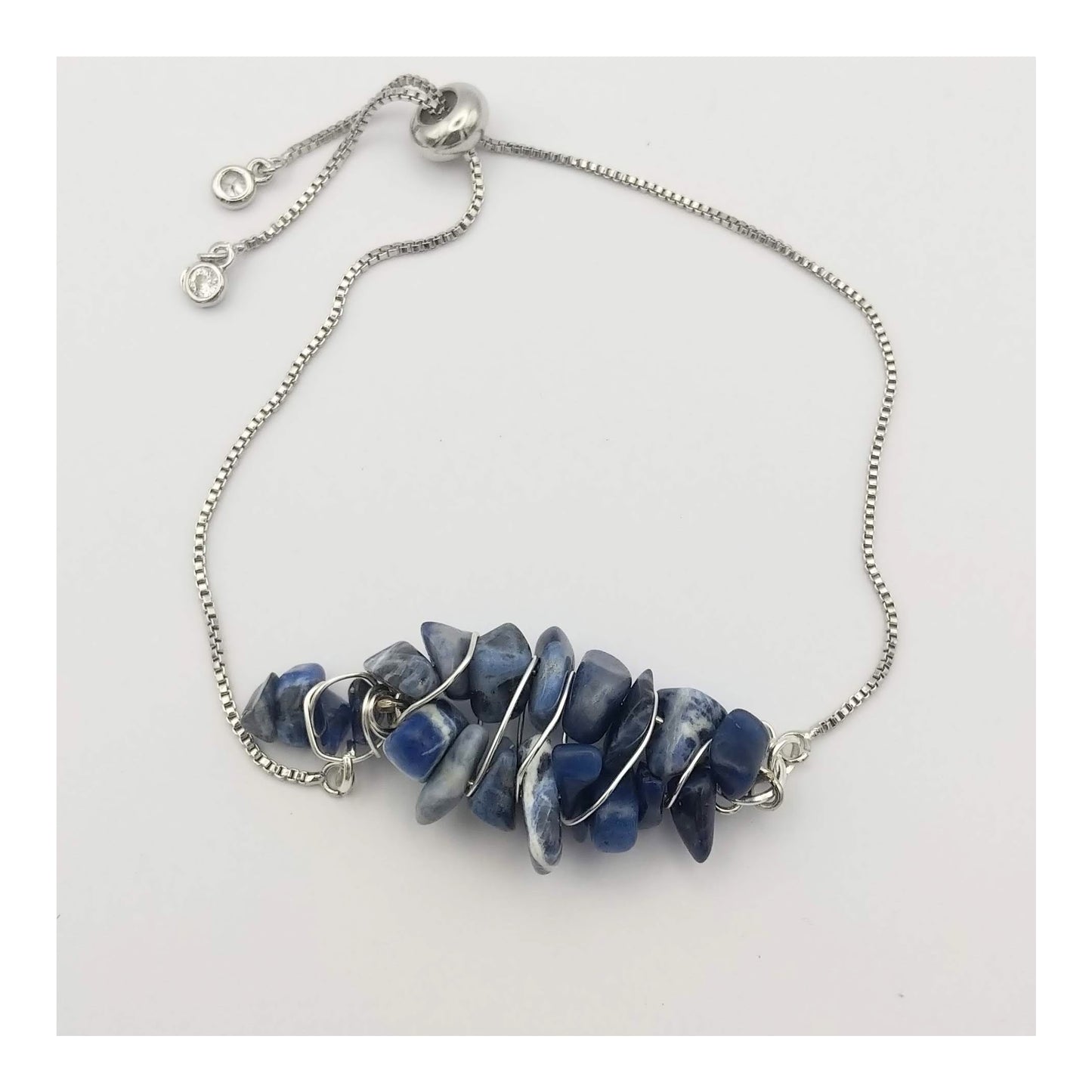 Adjustable bolo bracelet with small clear rhinestones on each end.  Linked to monochromatic blues and white sodalite chips strung on wire to form a flat almond shaped centerpiece, with silver toned wired spiraled around the sodalite chips.