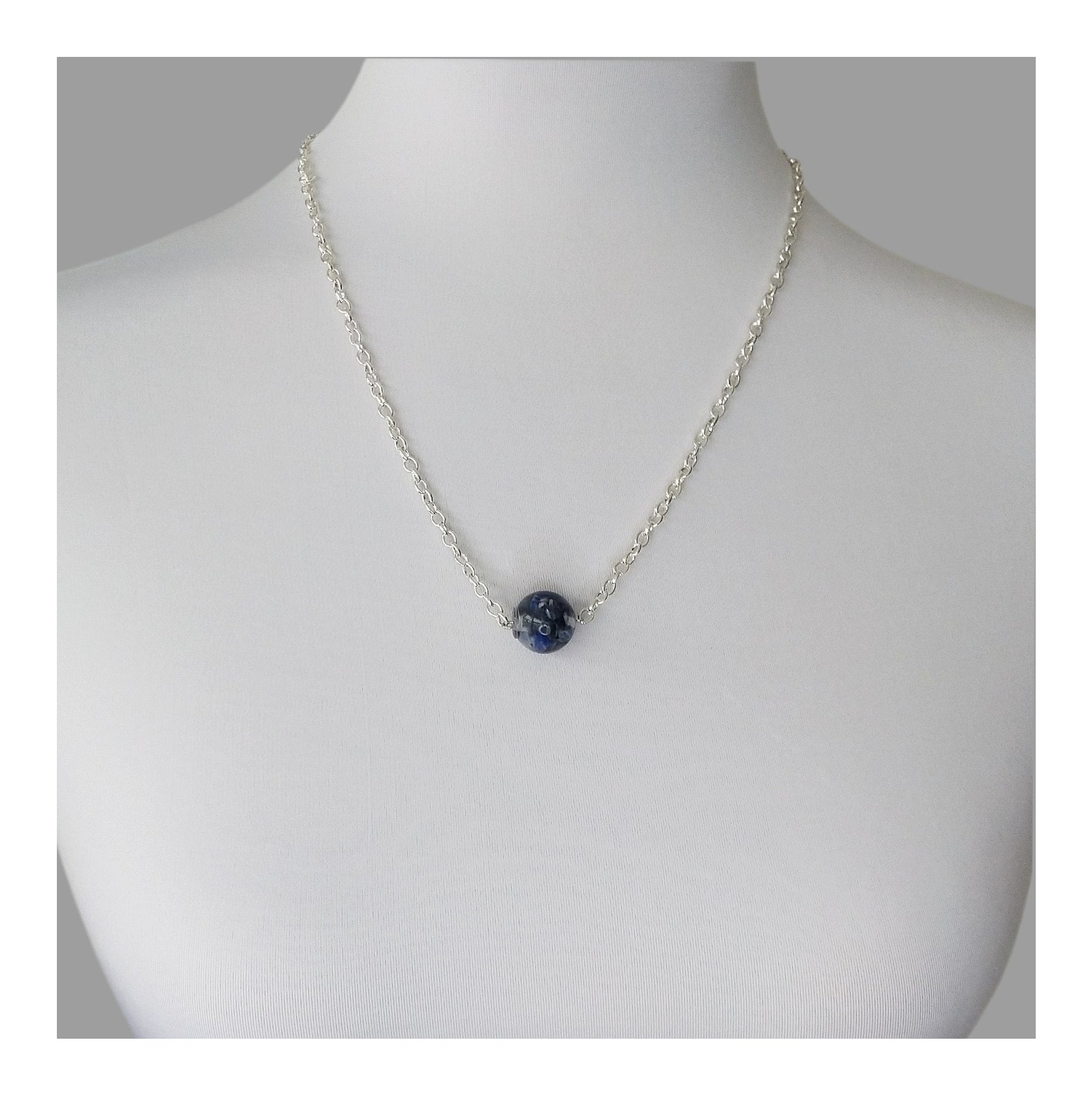 A ½ ich diameter single bead made of chipped sodalite encased in resin. Hanging from a 20 inch long silver toned chain.