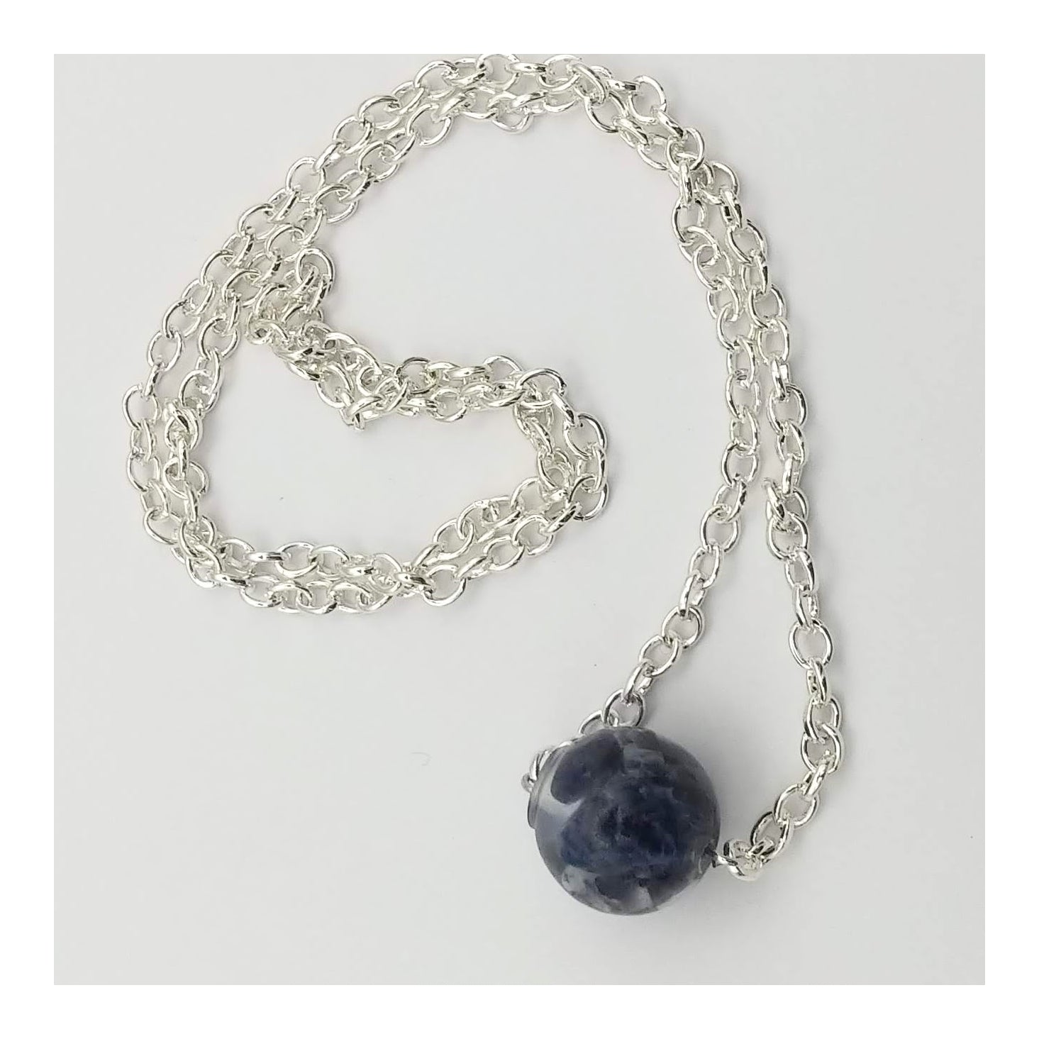 A ½ ich diameter single bead made of chipped sodalite encased in resin. Hanging from a 20 inch long silver toned chain.